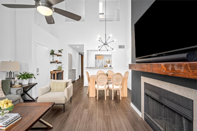 living room featuring wood finished floors, a towering ceiling, visible vents, a fireplace, and baseboards
