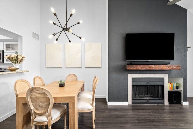 dining room featuring wood finished floors, a towering ceiling, visible vents, an inviting chandelier, and baseboards