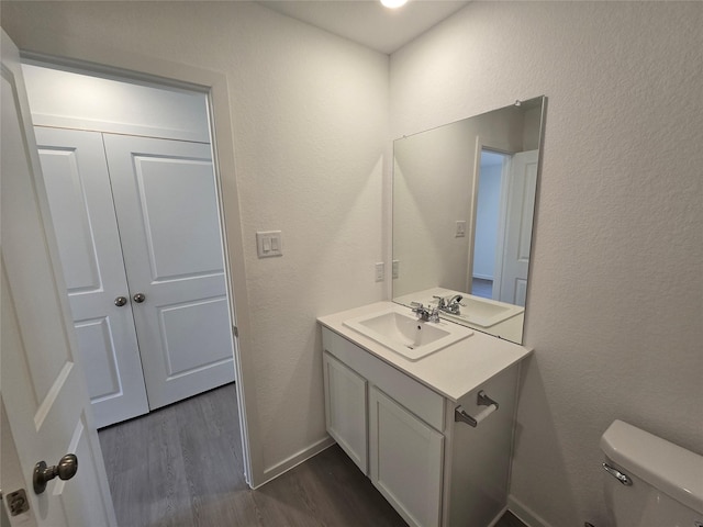 bathroom featuring wood finished floors, toilet, a textured wall, and vanity