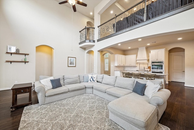 living area with dark wood-style flooring, ceiling fan, and arched walkways