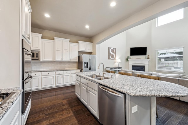 kitchen featuring white cabinetry, a sink, stainless steel appliances, open floor plan, and a kitchen island with sink