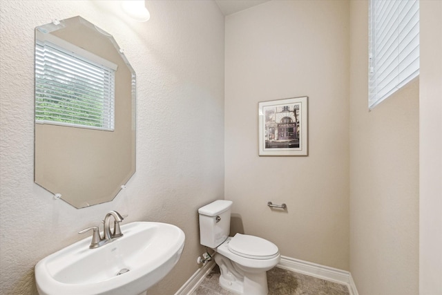 half bath featuring toilet, baseboards, and a sink