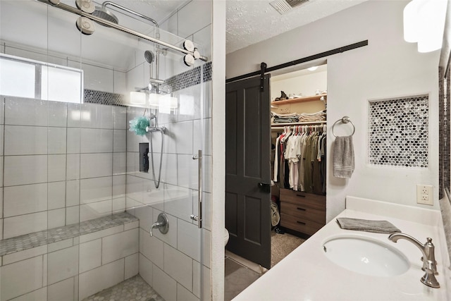 full bathroom with a textured ceiling, visible vents, a shower stall, vanity, and a spacious closet