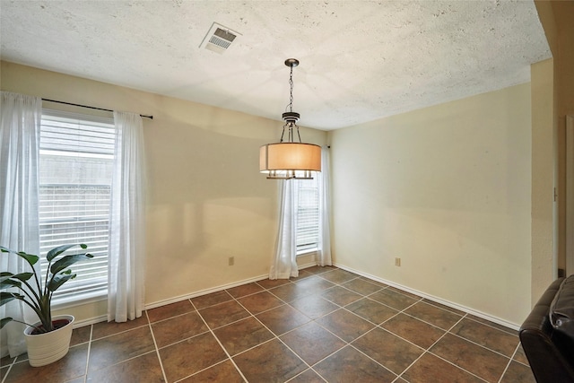 unfurnished dining area with visible vents, dark tile patterned floors, baseboards, and a wealth of natural light