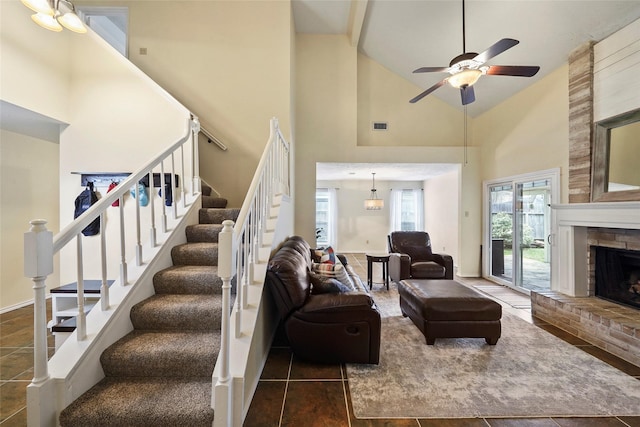 living area featuring a ceiling fan, visible vents, a fireplace, high vaulted ceiling, and stairs