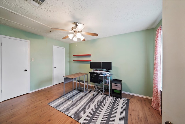 office space featuring ceiling fan, attic access, baseboards, wood finished floors, and visible vents