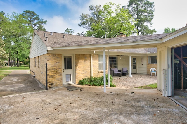 back of house featuring a chimney, brick siding, a shingled roof, and a patio area