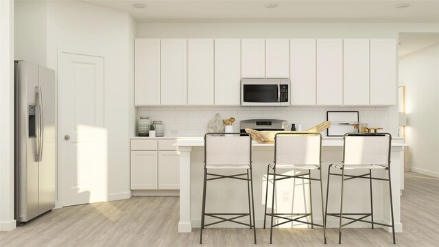 kitchen with light wood finished floors, stainless steel appliances, backsplash, light countertops, and an island with sink