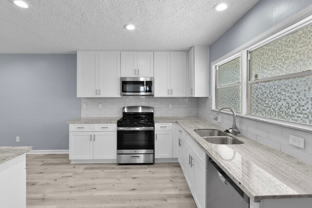 kitchen with a sink, light wood-type flooring, white cabinetry, a textured ceiling, and appliances with stainless steel finishes