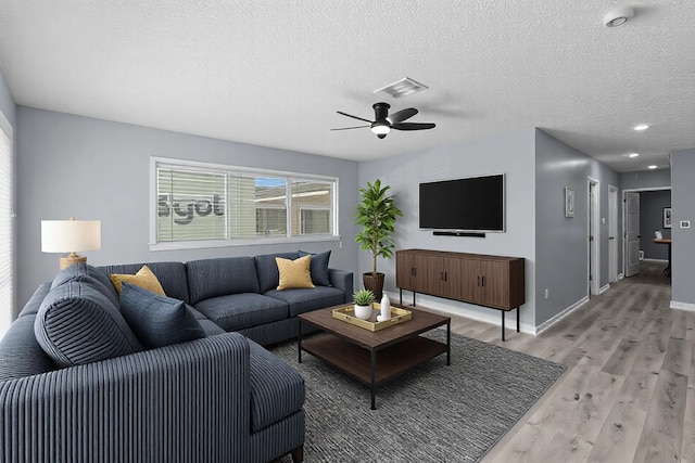 living room with a textured ceiling, ceiling fan, light wood finished floors, and baseboards