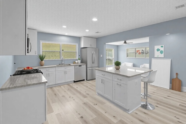 kitchen with a sink, stainless steel appliances, a kitchen bar, light wood-type flooring, and white cabinets