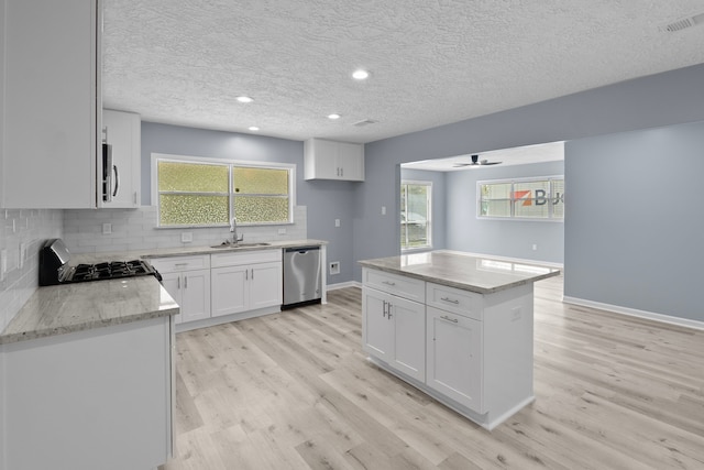 kitchen featuring light wood finished floors, light stone countertops, a sink, white cabinets, and appliances with stainless steel finishes