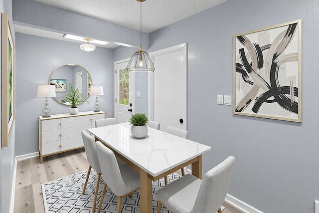 dining room with light wood finished floors, a textured ceiling, and baseboards