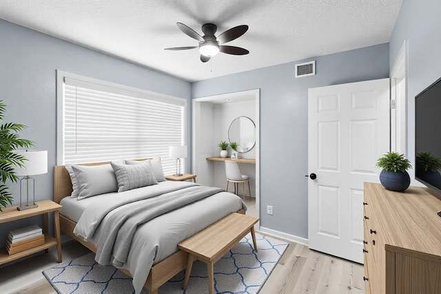 bedroom featuring a textured ceiling, visible vents, ceiling fan, light wood-style floors, and baseboards