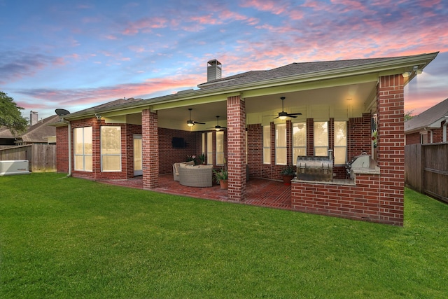 back of property at dusk with brick siding, a ceiling fan, a fenced backyard, and a yard
