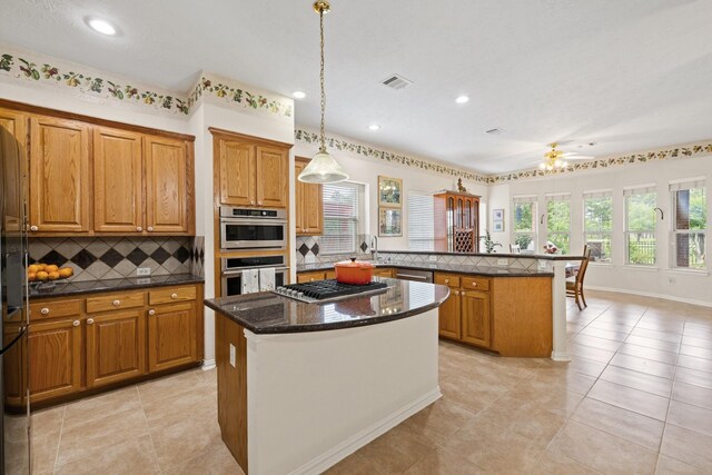 kitchen featuring brown cabinets, appliances with stainless steel finishes, a center island, a peninsula, and visible vents