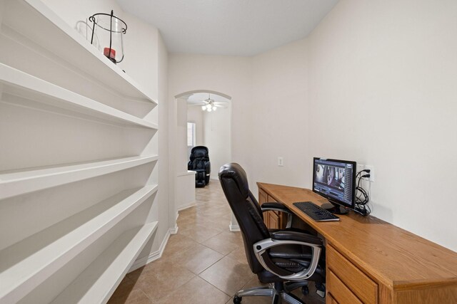 tiled office space featuring arched walkways, baseboards, and ceiling fan