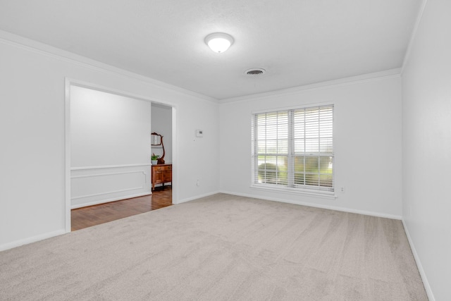 carpeted spare room featuring baseboards, visible vents, and crown molding