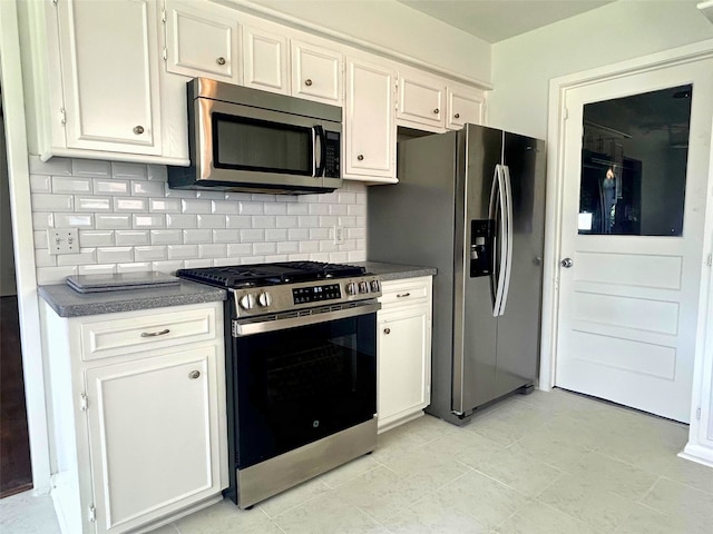 kitchen with dark countertops, white cabinets, stainless steel appliances, and tasteful backsplash