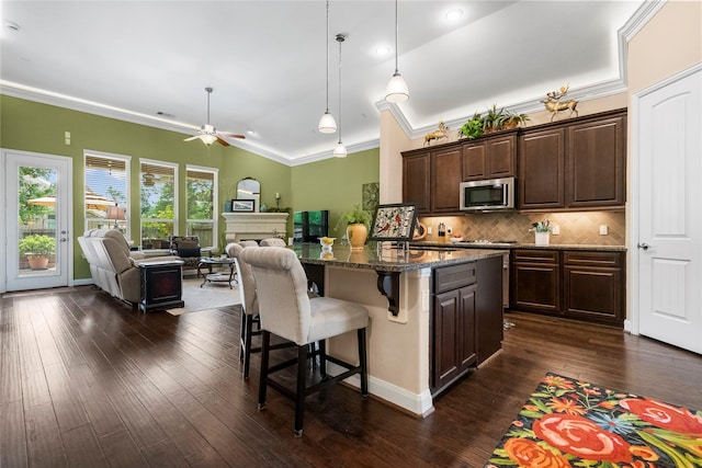 kitchen featuring open floor plan, a breakfast bar area, dark wood-style floors, stainless steel microwave, and a ceiling fan