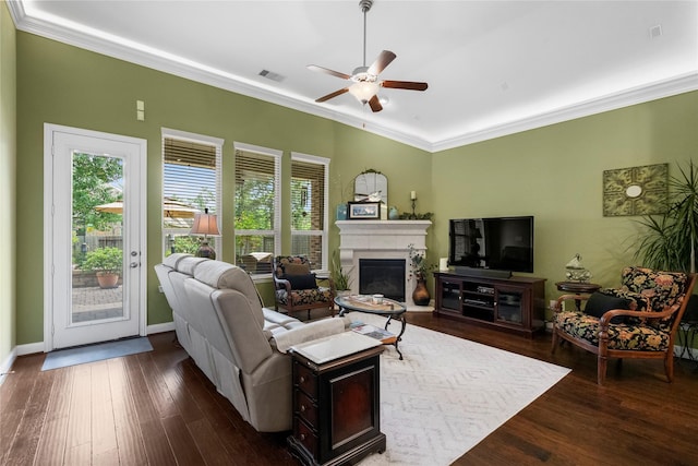 living area featuring crown molding, a glass covered fireplace, a ceiling fan, dark wood-type flooring, and visible vents