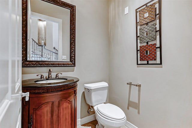 half bath with baseboards, toilet, and vanity