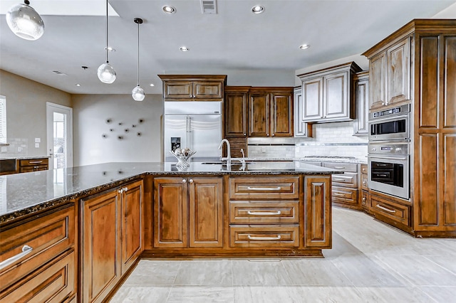 kitchen with dark stone counters, appliances with stainless steel finishes, a sink, visible vents, and pendant lighting