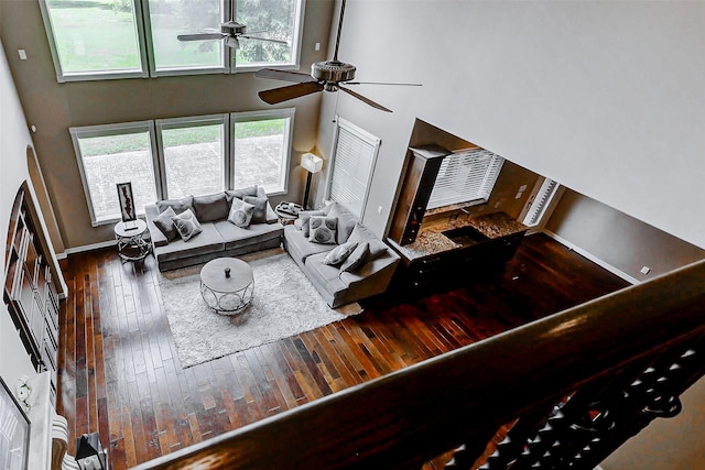 living area with a towering ceiling, a ceiling fan, baseboards, and wood-type flooring