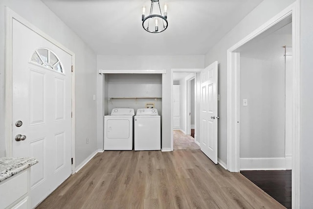 clothes washing area featuring independent washer and dryer, light wood-style floors, baseboards, an inviting chandelier, and laundry area