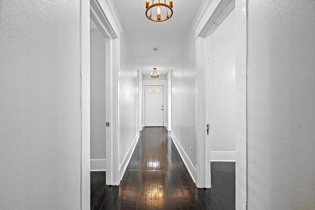 hallway with an inviting chandelier, a textured wall, hardwood / wood-style flooring, and baseboards