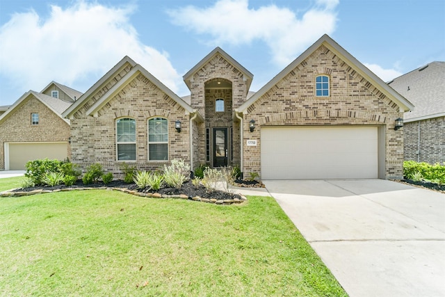 french country style house featuring a front lawn, driveway, an attached garage, and brick siding