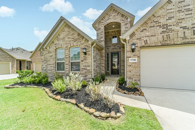 french country home featuring a garage, brick siding, a front yard, and concrete driveway