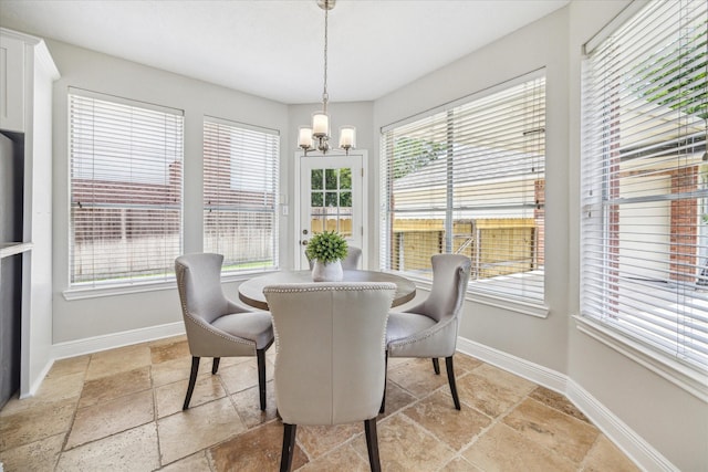 dining space featuring baseboards, a notable chandelier, and stone tile flooring