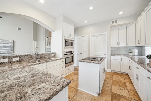 kitchen with visible vents, a center island, arched walkways, a sink, and appliances with stainless steel finishes