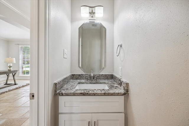 bathroom featuring vanity, ornamental molding, a textured wall, and stone tile floors