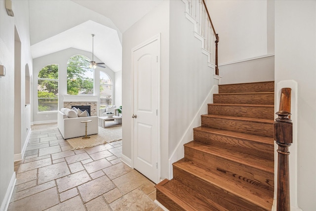 staircase with a fireplace, a ceiling fan, baseboards, lofted ceiling, and stone tile flooring