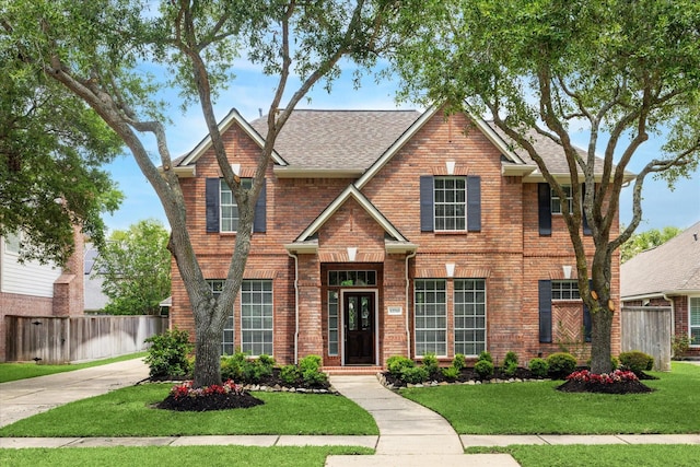 view of front of home with brick siding, fence, a front yard, and roof with shingles