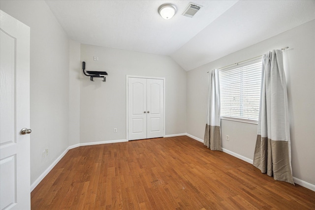 unfurnished bedroom featuring visible vents, baseboards, lofted ceiling, and wood finished floors