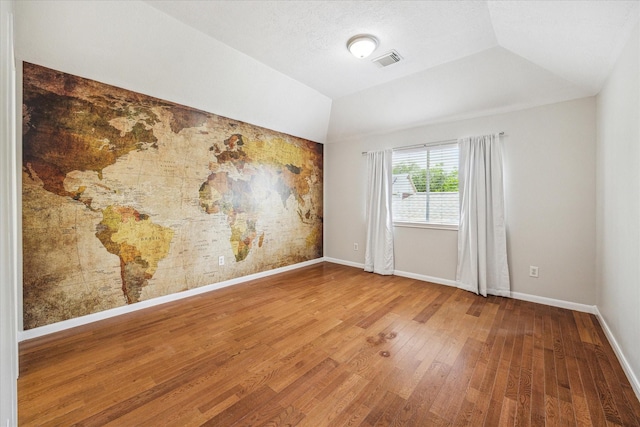 unfurnished room featuring baseboards, wood finished floors, visible vents, and vaulted ceiling