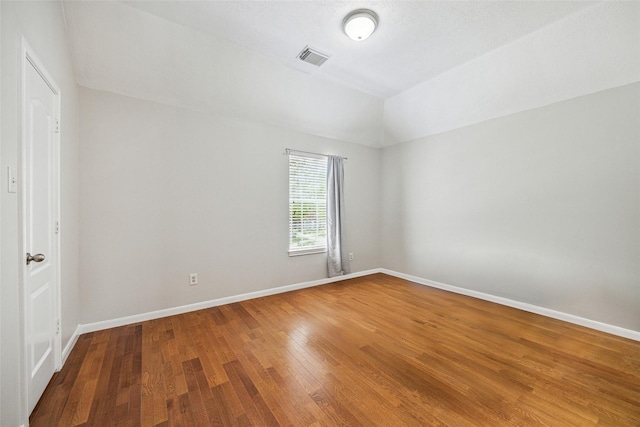 spare room with baseboards, vaulted ceiling, wood finished floors, and visible vents