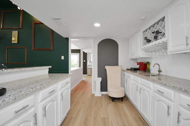 kitchen with a sink, light wood-style floors, visible vents, arched walkways, and white cabinets