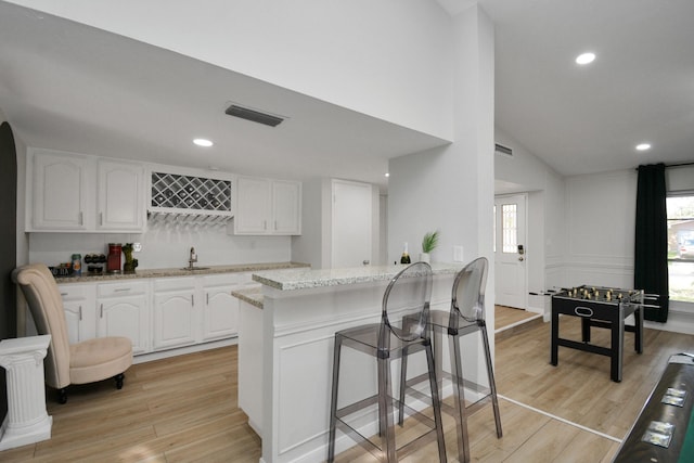 kitchen with white cabinetry, a sink, visible vents, light wood finished floors, and vaulted ceiling