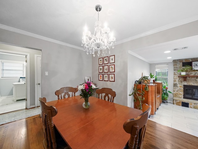 dining area featuring visible vents, wood finished floors, a stone fireplace, and ornamental molding