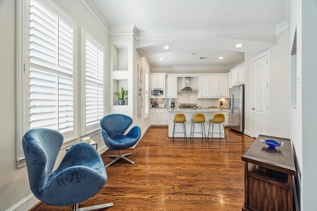 kitchen with ornamental molding, appliances with stainless steel finishes, a healthy amount of sunlight, and wall chimney range hood