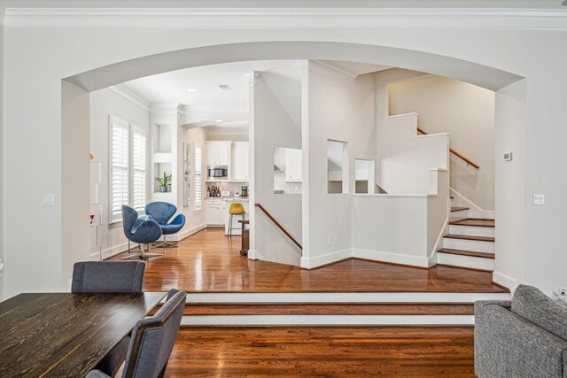interior space featuring arched walkways, wood finished floors, baseboards, ornamental molding, and stairs