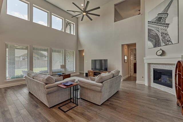 living room with a towering ceiling, ceiling fan, baseboards, and dark wood-type flooring