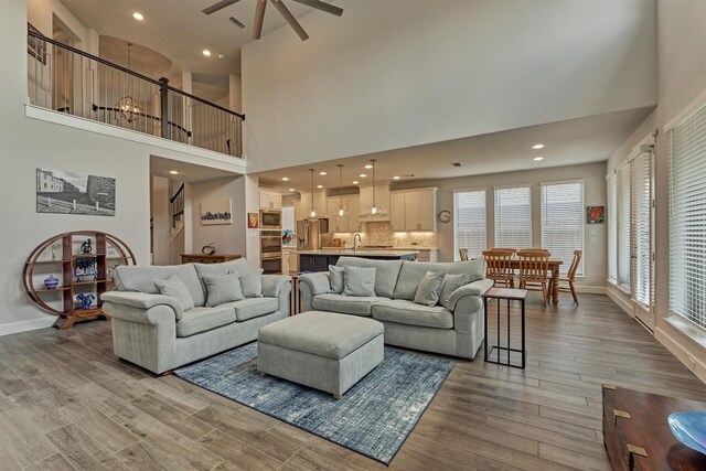 living room with baseboards, a ceiling fan, light wood-type flooring, and a towering ceiling