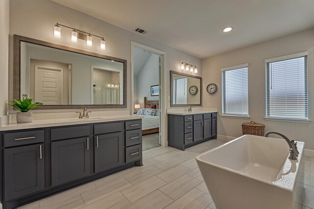 ensuite bathroom featuring visible vents, a sink, two vanities, and a soaking tub