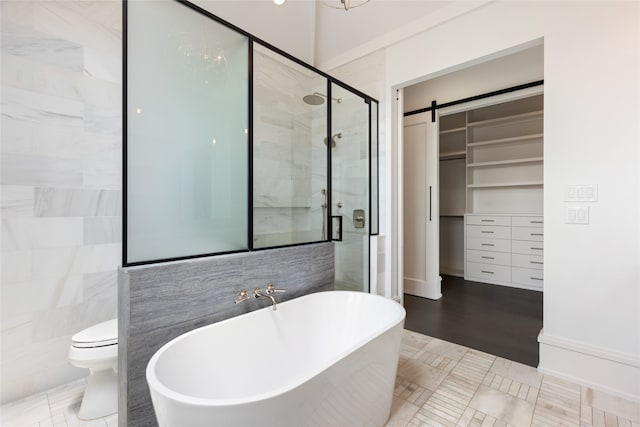 full bathroom featuring a walk in closet, a freestanding tub, tile walls, a stall shower, and toilet
