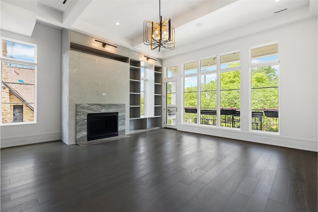 unfurnished living room featuring dark wood-style flooring, built in features, baseboards, a notable chandelier, and a premium fireplace